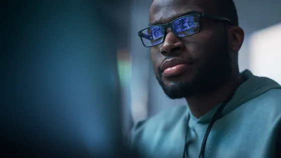 Image of man looking at computer screen reflected on glasses